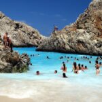 Spiaggia affollata con ombrelloni e persone che si godono la meta turistica più cliccata dell'anno.